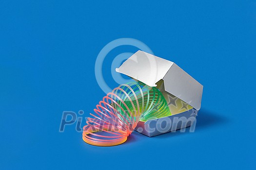 Plastic rainbow spring slinky toy in a silver colored food container on a blue background with soft shadows, copy space. Plastic rainbow spring slinky toy in a silver colored food container on a blue background with soft shadows, copy space.