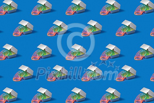 Patter made of Plastic rainbow spring slinky toy in a silver colored food container on a blue background with soft shadows, copy space. Patter made of Plastic rainbow spring slinky toy in a silver colored food container on a blue background with soft shadows, copy space.