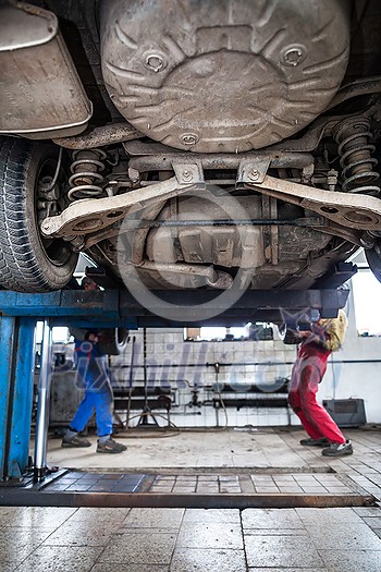 Inside a garage - two mechanics working on a car, changing wheels, doing maintenance (shallow DOF; color toned image) Inside a garage - two mechanics working on a car, changing wheels, doing maintenance (shallow DOF; color toned image)
