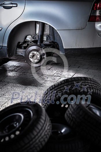 Modern car in a garage having its wheels/tires changed (shallow DOF; color toned image) Modern car in a garage having its wheels/tires changed (shallow DOF; color toned image)