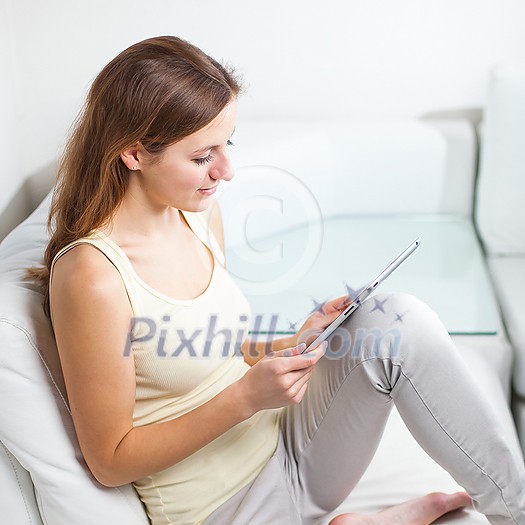 Pretty, young woman woman using digital tablet while relaxing on sofa at home. Attractive young woman wearing casual clothes. Pretty, young woman woman using digital tablet while relaxing on sofa at home. Attractive young woman wearing casual clothes.