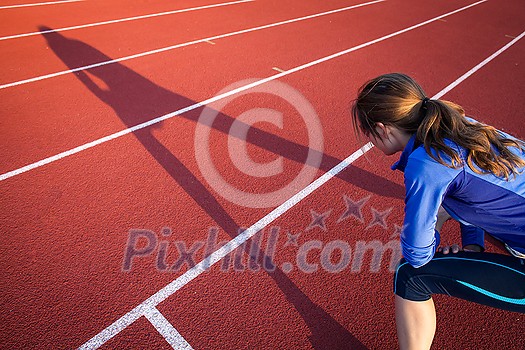 Pretty female runner stretching before her run at a track and field stadium Pretty female runner stretching before her run at a track and field stadium