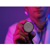 Portrait of hero in white coat.  Cheerful smiling young doctor with stethoscope in medical hospital standing against blue and pink background. Coronavirus covid-19 danger alert