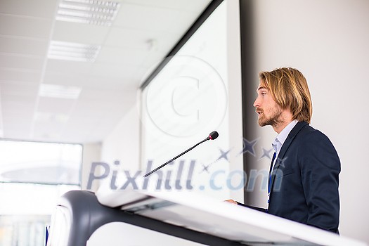 Handsome young man giving a speech at a conference Handsome young man giving a speech at a conference