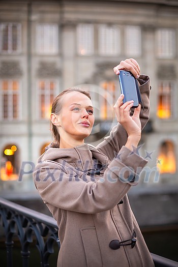 Elegant, young woman taking a photo with her cell phone camera while traveling (shallow DOF; color toned image) Elegant, young woman taking a photo with her cell phone camera while traveling (shallow DOF; color toned image)