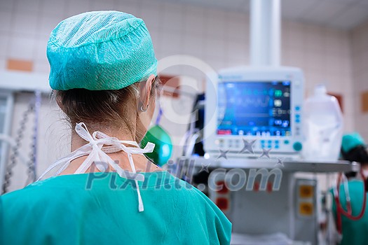 Female anesthesiologist with vital functions monitor in surgery room (color toned image; shallow DOF) Female anesthesiologist with vital functions monitor in surgery room (color toned image; shallow DOF)