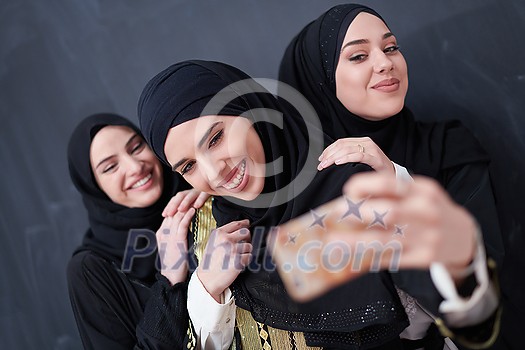 group of young beautiful muslim women in fashionable dress with hijab using mobile phone while taking selfie picture in front of black chalkboard representing modern islam fashion technology and ramadan kareem concept group of young beautiful muslim women in fashionable dress with hijab using mobile phone while taking selfie picture in front of black chalkboard representing modern islam fashion technology and ramadan kareem concept