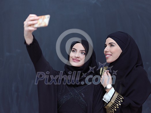 group of young beautiful muslim women in fashionable dress with hijab using mobile phone while taking selfie picture in front of black chalkboard representing modern islam fashion technology and ramadan kareem concept group of young beautiful muslim women in fashionable dress with hijab using mobile phone while taking selfie picture in front of black chalkboard representing modern islam fashion technology and ramadan kareem concept