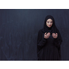 portrait of beautiful muslim woman in fashionable dress with hijab making traditional prayer to God, keeps hands in praying gesture isolated on black chalkboard background representing modern islam fashion and ramadan kareem concept