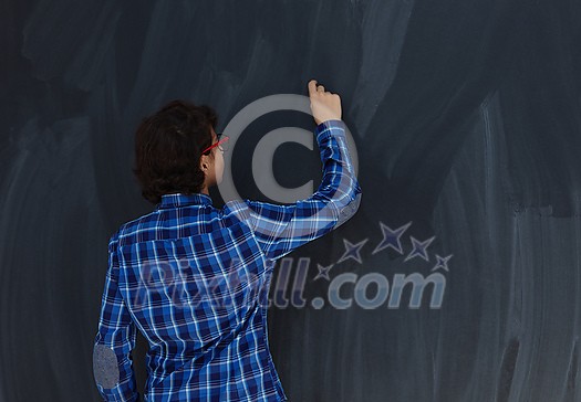 Smart Arab Teen Boy with chalk in hand writing on empty black board in school Smart Arab Teen Boy with chalk in hand writing on empty black board in school