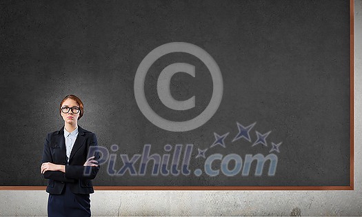 Young confident woman wearing glasses standing near blank blackboard Young confident woman wearing glasses standing near blank blackboard