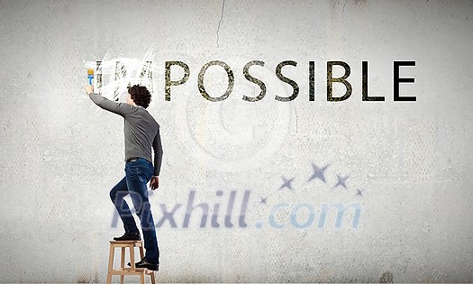 Man changing word impossible in to possible by erasing part of word with paint brush Man changing word impossible in to possible by erasing part of word with paint brush