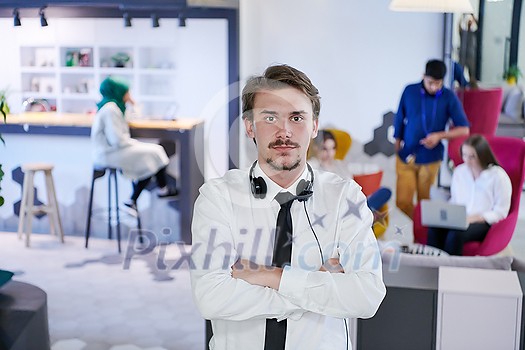 portrait of successful businessman entrepreneur with headphones around his neck and colleagues in the background at busy startup office portrait of successful businessman entrepreneur with headphones around his neck and colleagues in the background at busy startup office