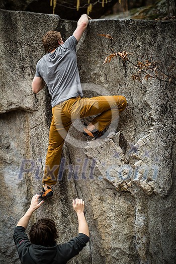 A rock climber climbing on a boulder rock outdoors. Group of friends involved in sports outside.