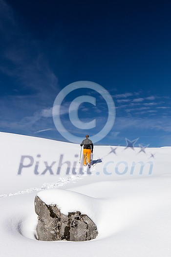 Winter sports - young man walking with snowshoes uphill in high mountains covered with lots of snow (selective focus on the mountain in the background)