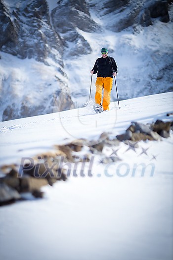 Winter sports - young man running with snowshoes downhill in high mountains covered with lots of snow