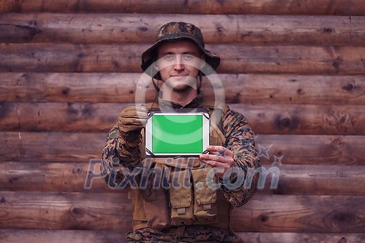 Soldier using tablet computer against old wooden wall in military camp to stay in contact with friends and family Soldier using tablet computer against old wooden wall in military camp to stay in contact with friends and family