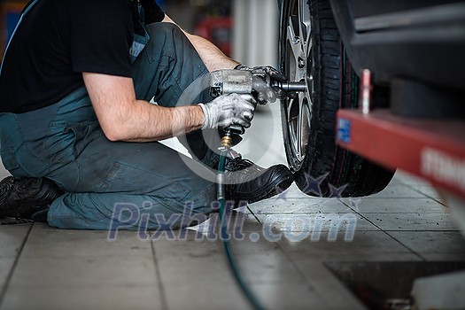 Car mechanic changind tires of a car in a repair shop/car garage (shallow DOF/color toned image) Car mechanic changind tires of a car in a repair shop/car garage (shallow DOF/color toned image)