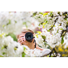 Pretty, female photographer outdoors on a lovely spring day, taking pictures of a blossoming tree