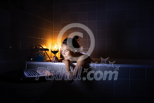 Young woman taking a bath, drinking red wine, enjoying a movie, relaxing after busy work day Young woman taking a bath, drinking red wine, enjoying a movie, relaxing after busy work day