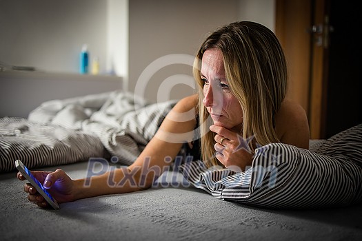 Pretty, middle-aged woman using her tablet computer before sleep in bed in the evening Pretty, middle-aged woman using her tablet computer before sleep in bed in the evening