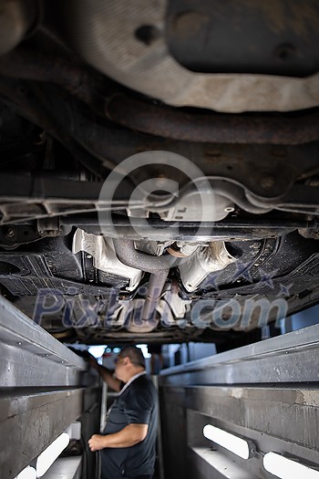 Car mechanic under a car in a repair shop/car garage (shallow DOF/color toned image) Car mechanic under a car in a repair shop/car garage (shallow DOF/color toned image)