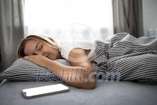 Pretty, young woman sleeping in her bed with her cell phone close to her. Smartphone in Bed Mobile/smartphone Addiction Concept. Pretty, young woman sleeping in her bed with her cell phone close to her. Smartphone in Bed Mobile/smartphone Addiction Concept.