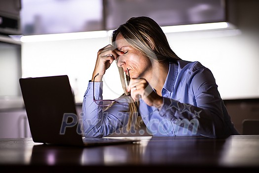 Pretty, middle-aged woman working late in the day on a laptop computer at home, running a business from home/working remotely - getting frustrated Pretty, middle-aged woman working late in the day on a laptop computer at home, running a business from home/working remotely - getting frustrated