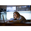 Middle-aged woman working late in the day on a laptop computer at home, running a business from home/working remotely for a corporation