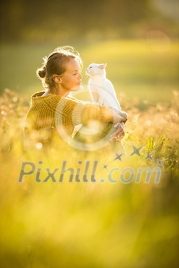 Pretty, young woman with her cat pet sitting in grass on lovely meadow lit by warm evening light (shallow DOF; color toned image) Pretty, young woman with her cat pet sitting in grass on lovely meadow lit by warm evening light (shallow DOF; color toned image)