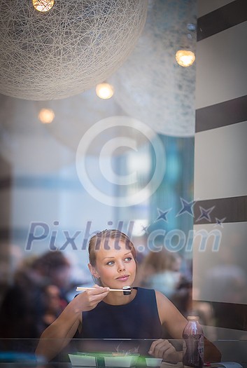 Pretty, young woman eating sushi in a restaurant, having her lunch break, enjoying the food, pausing for a while from her busy corporate/office life (color toned image) Pretty, young woman eating sushi in a restaurant, having her lunch break, enjoying the food, pausing for a while from her busy corporate/office life (color toned image)