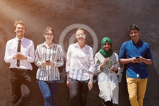 multiethnic group of casual business people using mobile phone during break from work in front of gray wall outside multiethnic group of casual business people using mobile phone during break from work in front of gray wall outside