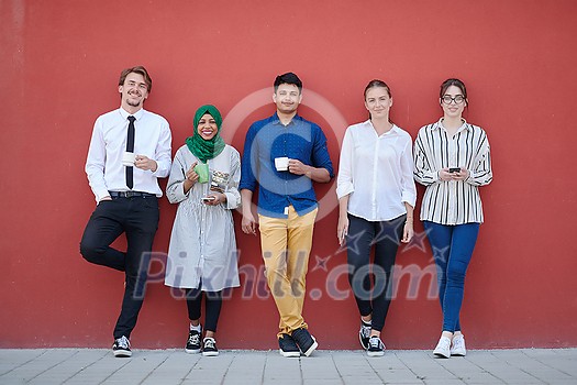 multiethnic group of casual business people using mobile phone during coffee break from work in front of pink wall outside multiethnic group of casual business people using mobile phone during coffee break from work in front of pink wall outside