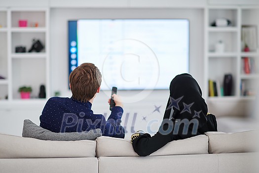 young muslim couple woman wearing islamic hijab clothes sitting on sofa watching TV together during the month of Ramadan at modern home young muslim couple woman wearing islamic hijab clothes sitting on sofa watching TV together during the month of Ramadan at modern home