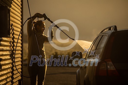 Cute woman washing her car in a manual carwash (color toned image) Cute woman washing her car in a manual carwash (color toned image)