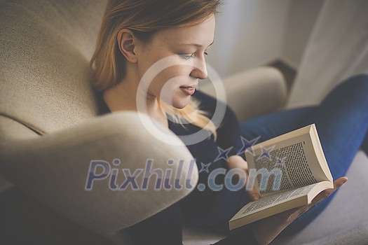 Cute young woman reading a book in a designer chair - color toned image, shallow DOF Cute young woman reading a book in a designer chair - color toned image, shallow DOF