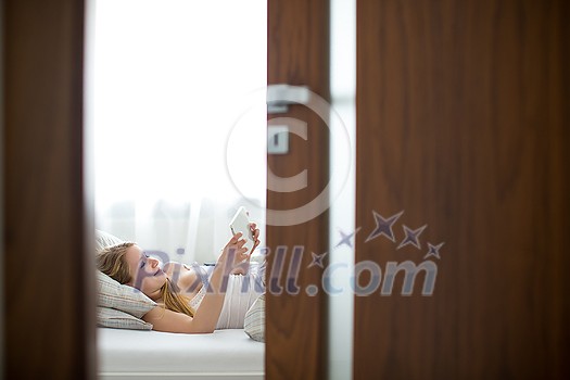Pretty, young woman in her bed, using a tablet computer in the morning Pretty, young woman in her bed, using a tablet computer in the morning