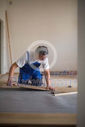 DIY, repair, building and home concept - Senior landlord lying parquet floor board/laminate flooring in a rental appartement (shallow DOF; color toned image) DIY, repair, building and home concept - Senior landlord lying parquet floor board/laminate flooring in a rental appartement (shallow DOF; color toned image)