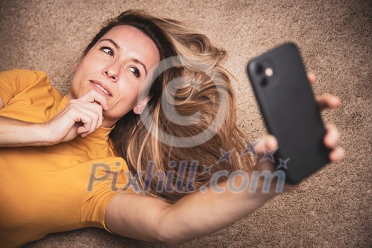 Happy mid-aged woman taking selfie with her smart phone at home Happy mid-aged woman taking selfie with her smart phone at home