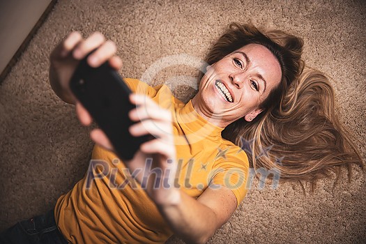 Happy mid-aged woman taking selfie with her smart phone at home Happy mid-aged woman taking selfie with her smart phone at home