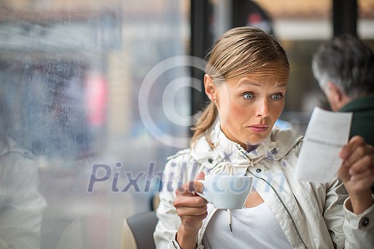 Pretty, young woman baffled with the bill in a coffeeshop/restaurant Pretty, young woman baffled with the bill in a coffeeshop/restaurant