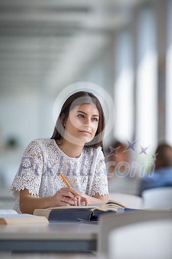 Pretty, young college student looking for a book in the library, studying for her exam Pretty, young college student looking for a book in the library, studying for her exam