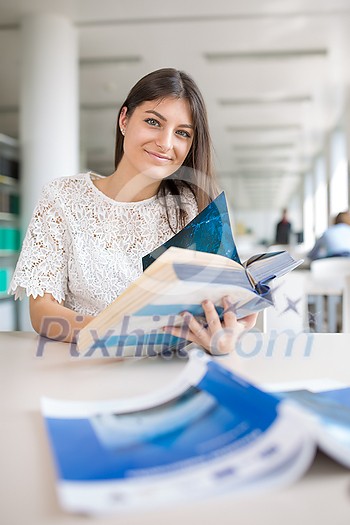 Pretty, young college student looking for a book in the library, studying for her exam Pretty, young college student looking for a book in the library, studying for her exam