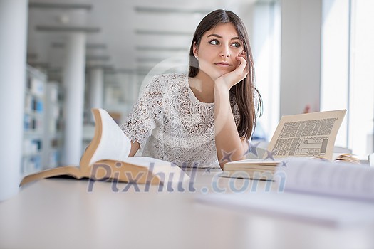 Pretty, young college student looking for a book in the library, studying for her exam Pretty, young college student looking for a book in the library, studying for her exam