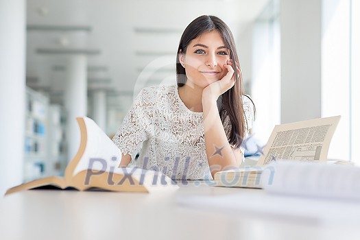 Pretty, young college student looking for a book in the library, studying for her exam Pretty, young college student looking for a book in the library, studying for her exam