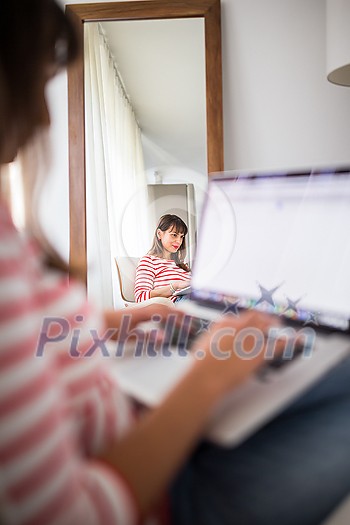 Successful young business woman sitting in a designer chair, working from home. Portrait of happy entrepreneur working on a laptop computer. Doing business remotely from the comfort of her home.