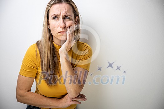 Mid-aged woman touching her cheek/mouth with painful expression because of toothache/dental issue Mid-aged woman touching her cheek/mouth with painful expression because of toothache/dental issue