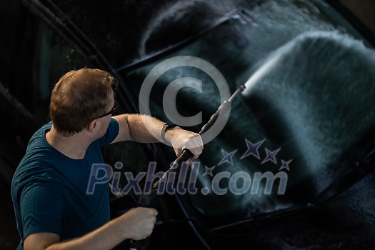 Young man washing his beloved car carefully in a manual car wash to prevent any damage and detail it properly Young man washing his beloved car carefully in a manual car wash to prevent any damage and detail it properly