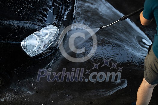 Young man washing his beloved car carefully in a manual car wash to prevent any damage and detail it properly Young man washing his beloved car carefully in a manual car wash to prevent any damage and detail it properly