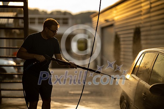 Young man washing his beloved car carefully in a manual car wash to prevent any damage and detail it properly Young man washing his beloved car carefully in a manual car wash to prevent any damage and detail it properly